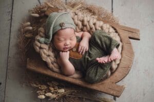 Newborn baby boy in green farmer outfit posing like a boss in rustic wood dough bowl