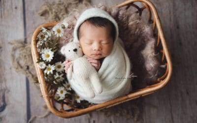 Newborn Photography Singapore | Meadow Lullabies Gently wrapped newborn sleeping in a rattan basket adorned with white daisies, newborn photography Singapore