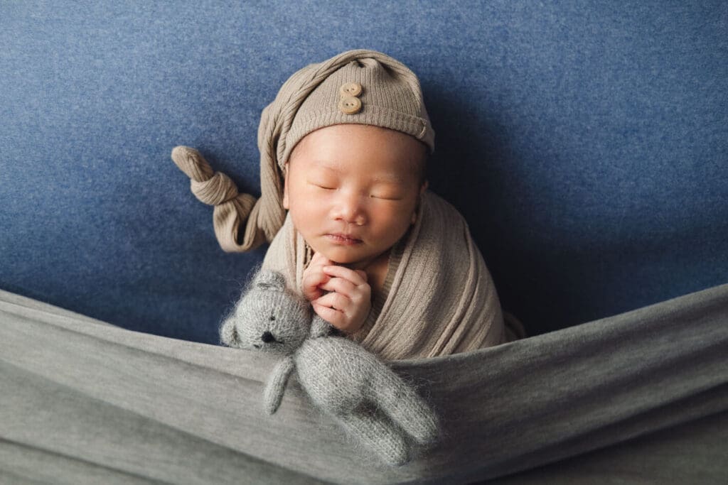 Newborn photography baby in khaki wraps holding bear soft toy