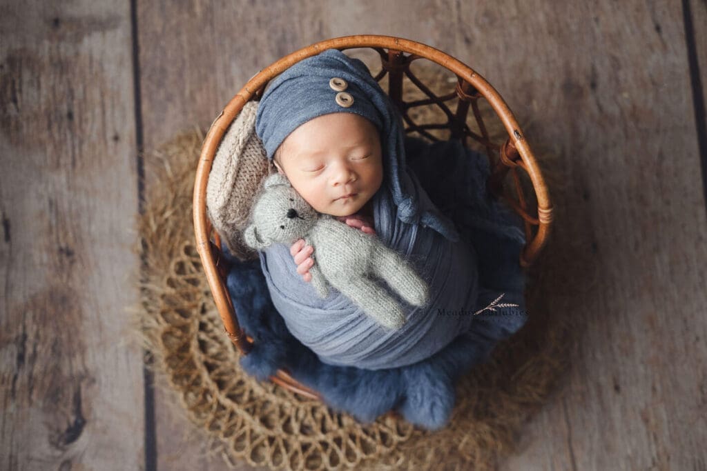 Newborn photography baby holding bear soft toy posing on vintage rattan stool