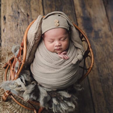 Newborn baby wrapped in grey on vintage rattan chair