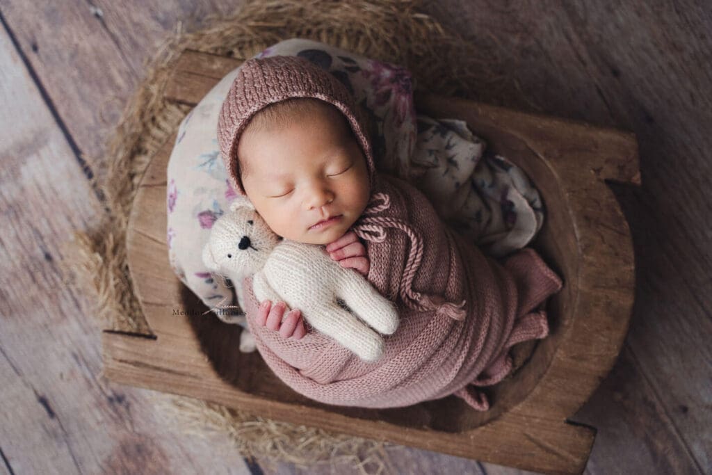 Newborn baby girl holding soft toy bear in crate prop