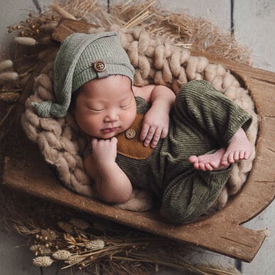 Newborn photoshoot baby sleeping in rustic bowl in green jumper outfit
