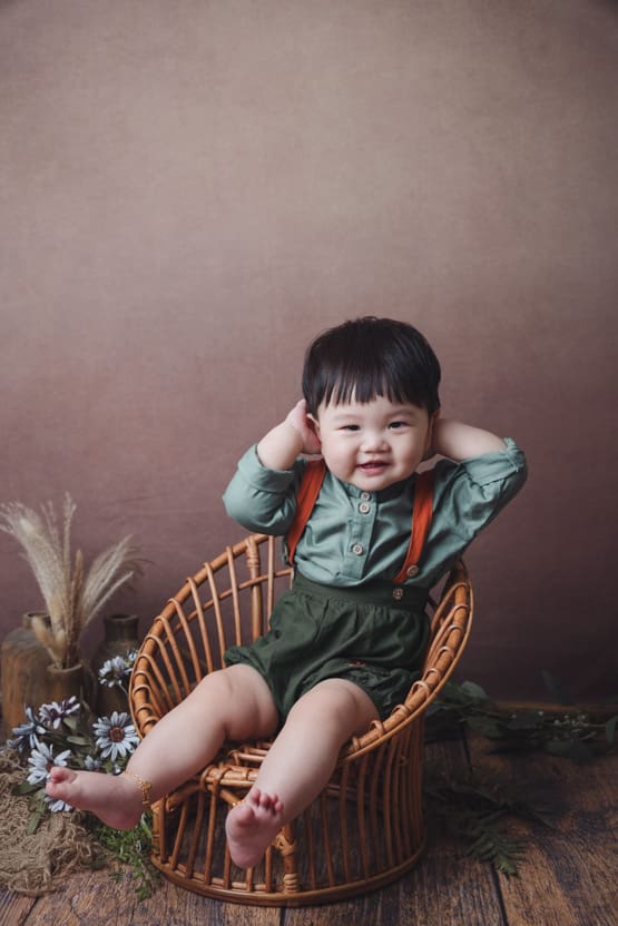 Baby photoshoot: 10 months old cupping his ears sitting on vintage rattan chair