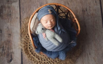 Baby Photoshoot, newborn in blue wrap clutching a mini bear soft toy on a vintage stool prop