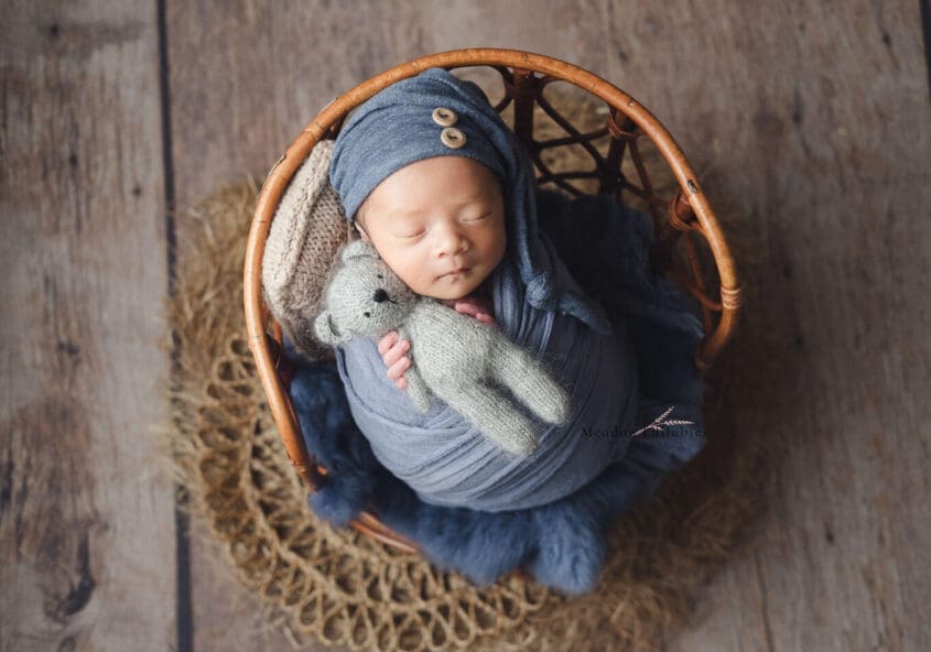 Baby Photoshoot, newborn in blue wrap clutching a mini bear soft toy on a vintage stool prop