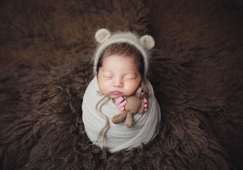 Newborn baby bundle up holding a bear soft toy